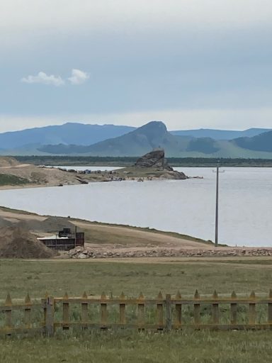 Weite Landschaft mit Wasser, Bergen und einem Fahrzeug am Ufer.